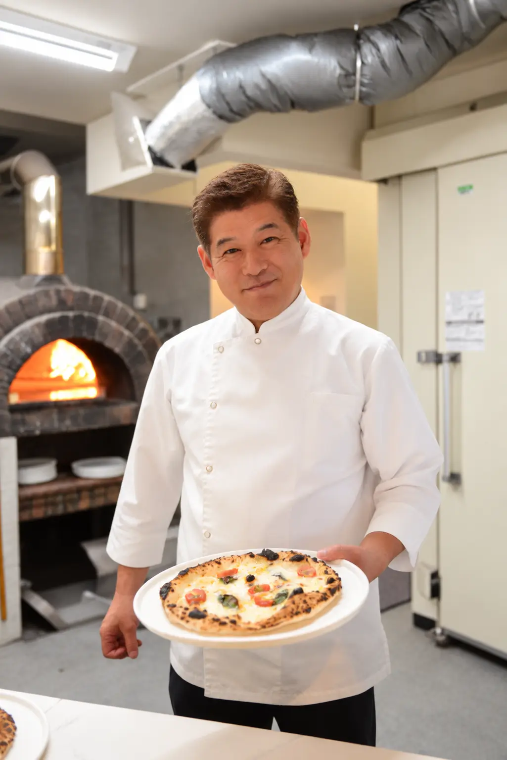石窯の前で焼き上がったピザを手にする代表の矢野竜二郎